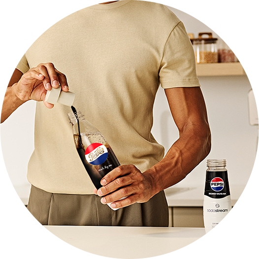 Mężczyzna nalewa własnoręcznie przygotowaną Pepsi z butelki SodaStream prosto do szklanki z kostkami lodu