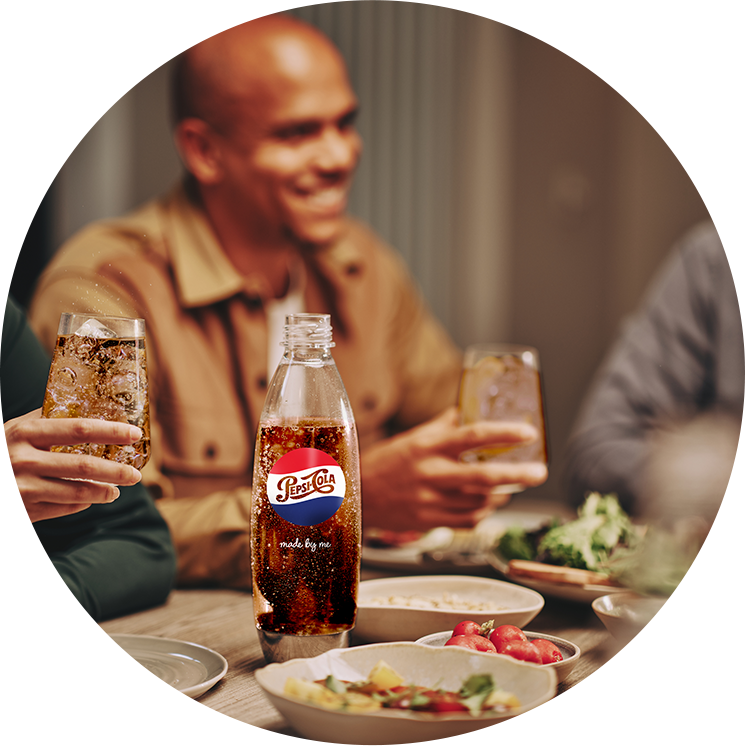 Butelka SodaStream Fuse Pepsi Made by You pełna Pepsi, stojąca na stole wśród potraw i sałatek przy spotkaniu ze znajomymi