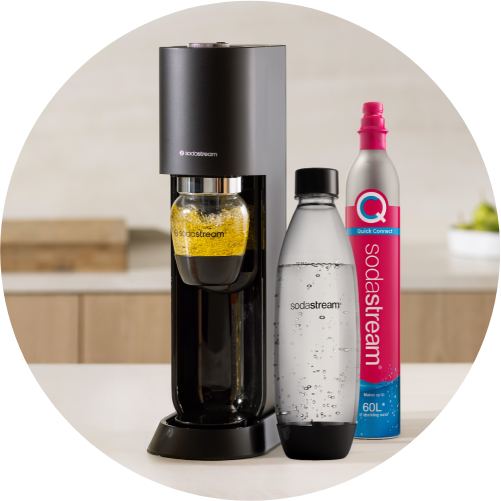 Maszyna SodaStream z czarną obudową, butelką z żółtym napojem i  butelką wody gazowanej, obok pojemnik Quick Connect 60L