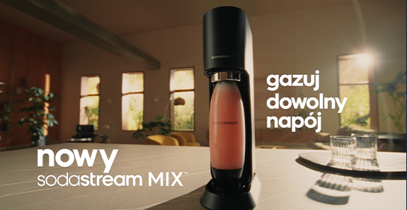 Nowa maszyna SodaStream MIX z różowym napojem na stole, jasne wnętrze z oknami i tekstem "gazuj dowolny napój"