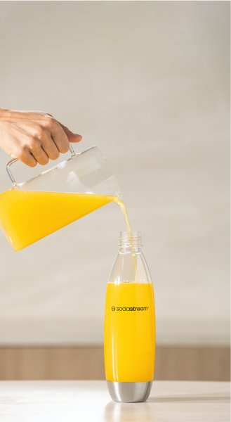 Wlewanie pomarańczowego napoju z dzbanka do butelki SodaStream na blacie
