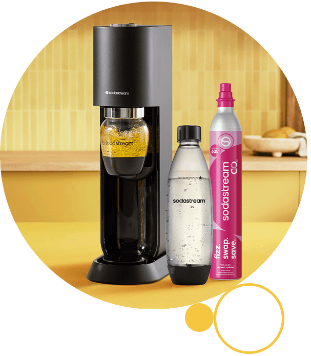 Maszyna Sodastream z czarną obudową, butelką z żółtym napojem i  butelką wody gazowanej, obok pojemnik Quick Connect 60L