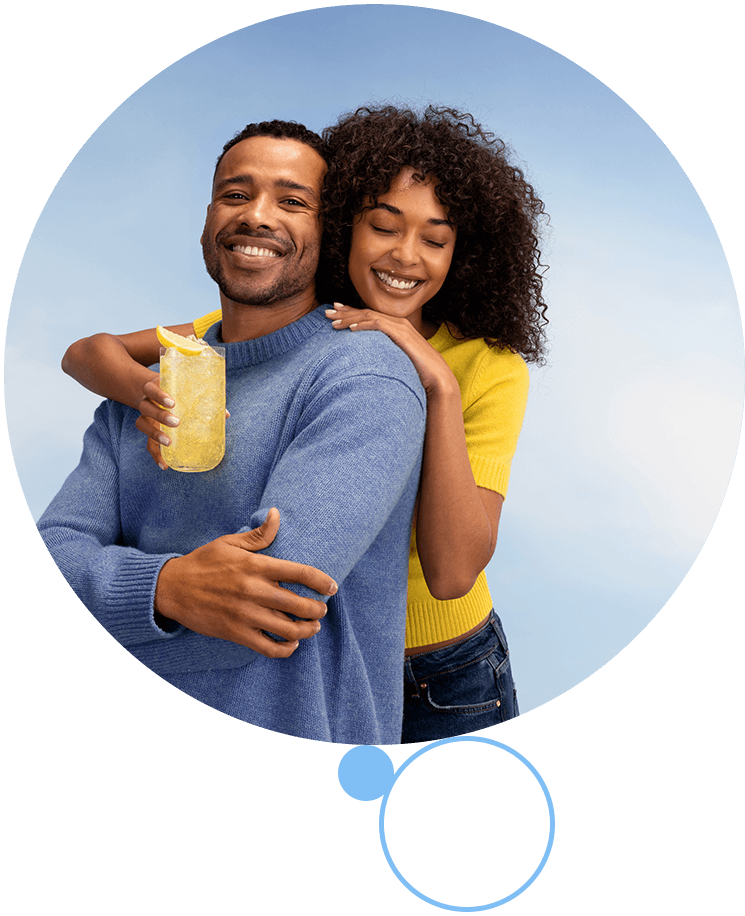 Maszyna Sodastream&nbsp;MIX z mężczyzną nasycającym napój, kobietą trzymającą pomarańczowy koktajl i kieliszkiem wina na blacie