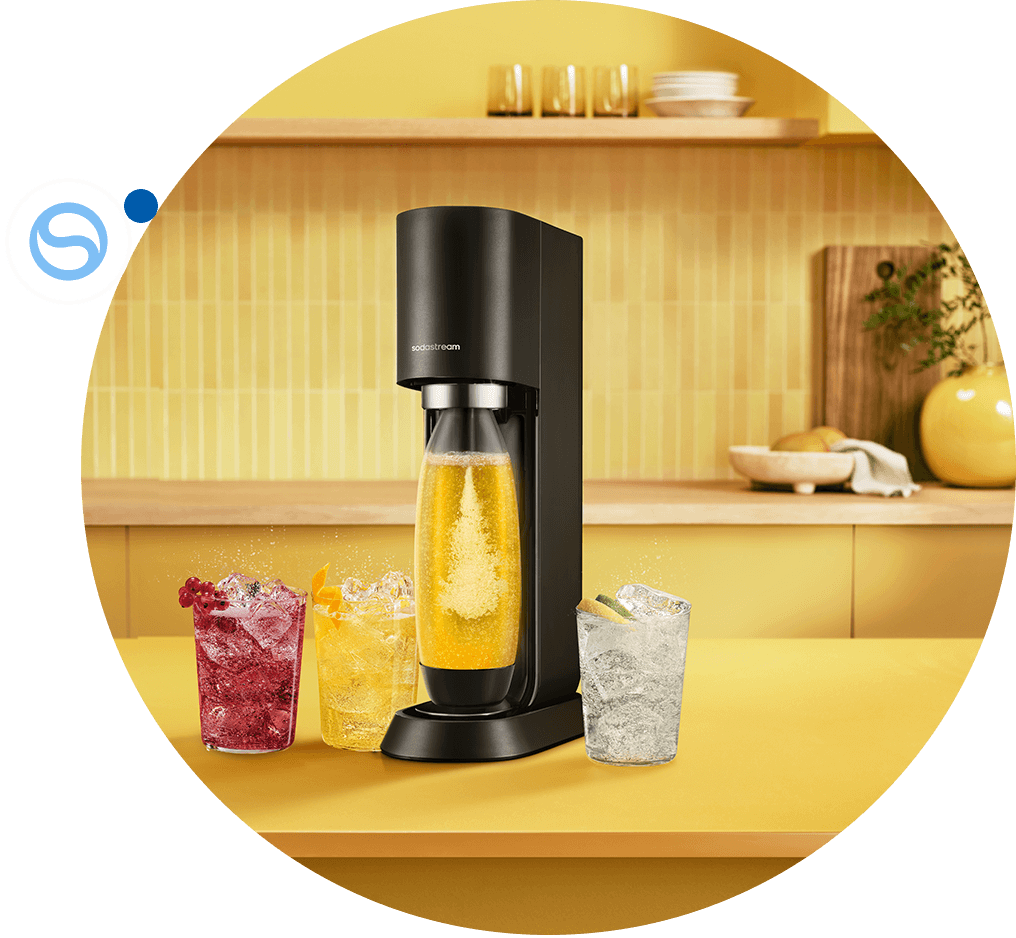 Kobieta w niebieskiej bluzce obsługująca czarną maszynę Sodastream z butelką pomarańczowego napoju, obok dzbanek i szklanka